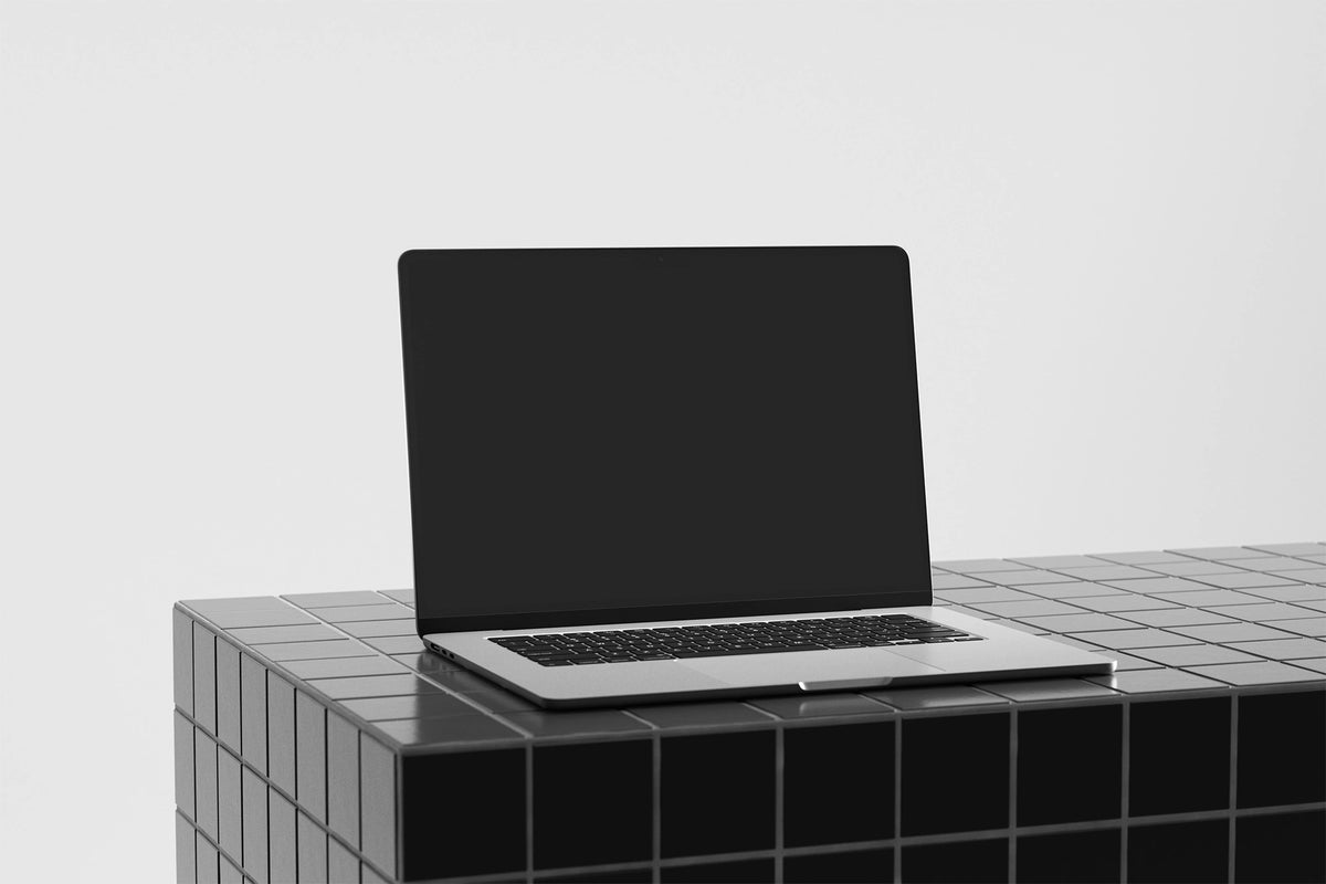 Laptop mockup on a gray tile table with a black UI placeholder for web and desktop UI presentation, angled view